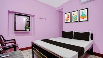 Un dormitorio con cama, una silla, una mesita, una ventana con planta y tres cuadros en la pared.