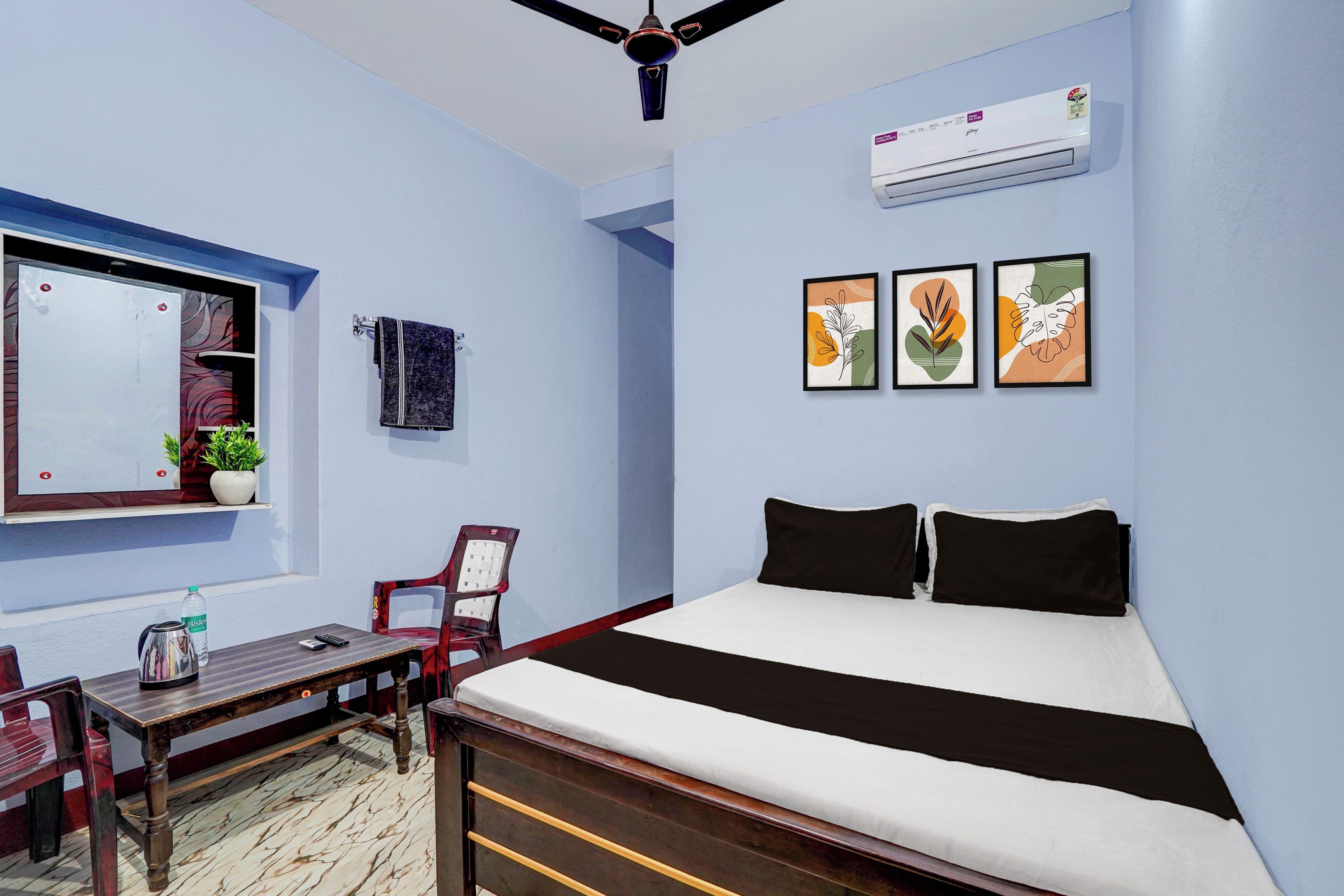 Ein Schlafzimmer mit einem Bett, einem Schreibtisch, einem Stuhl, einer Topfpflanze und Wandbildern.