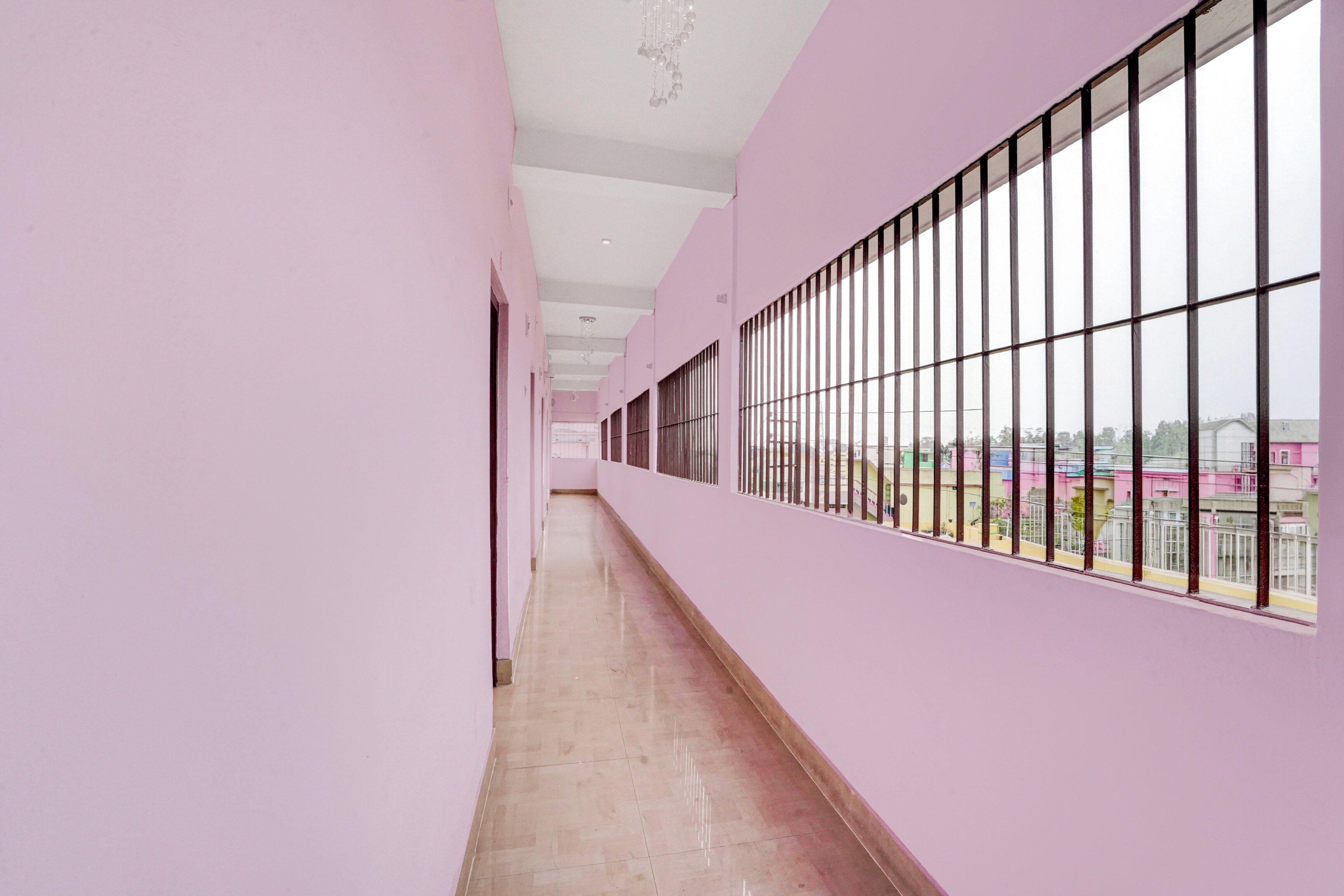 A corridor with pink walls, a tiled floor, and large windows with metal bars.