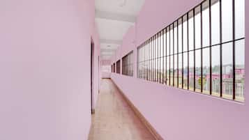 A corridor with pink walls, a tiled floor, and large windows with metal bars.