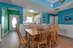 A dining area with a wooden table and chairs, a kitchen in the background, and a bright blue wall. - Siesta Key Beach | Heated Pool, Spa & Lock-Off Suite (Siesta Key)