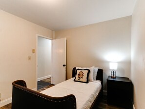 Een slaapkamer met een bed, een nachtkastje, een stoel en een deur naar een andere kamer.
