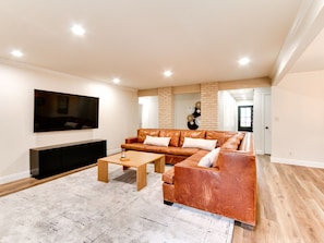 A modern living room with a leather sofa, a coffee table, and a flat-screen TV mounted on the wall. - Spacious 6-bedroom house in serene Tulsa with cool AC (Tulsa)