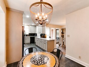 A dining area with a round table featuring a geometric pattern, a chandelier, and a kitchen in the background. - Spacious 6-bedroom house in serene Tulsa with cool AC (Tulsa)
