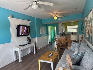 A living room with a television, a dining area with chairs, a sofa, and a kitchen in the background. - Siesta Key Lock-Off: Studio + 2BR, Pool & Walk to Beach & Village (Siesta Key)