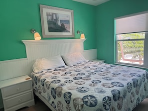 A bedroom with a bed, two bedside tables, a nightstand, a window with a view, and a framed picture on the wall. - Siesta Key Lock-Off: Studio + 2BR, Pool & Walk to Beach & Village (Siesta Key)