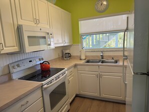 A kitchen with white cabinets, a microwave, a stove, a kettle, a coffee maker, and a sink. - Exclusive Second-Floor Retreat | Pool, Spa & Near Siesta Key Beach (Siesta Key)