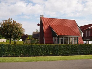 Ein Haus mit rotem Satteldach, einer Satellitenschüssel und einer Hecke davor.