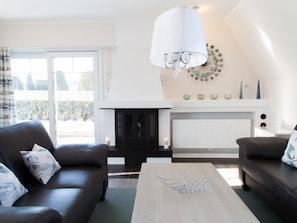 A living room with a fireplace, a sofa, a coffee table, and a chandelier. - Captain's Dream Cabin (Wittmund)