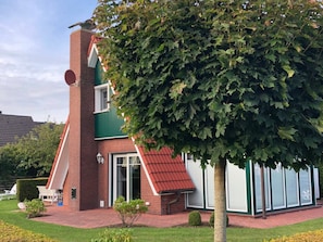 A two-story building with a brick facade, a red-tiled roof, and a large tree in front. - Captain's Dream Cabin (Wittmund)