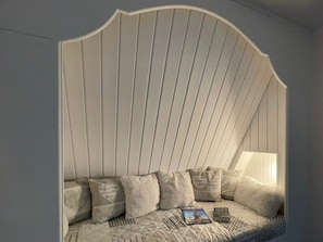 A cozy reading nook with a curved headboard, a patterned throw blanket, and a book titled 'OSTFRIESLAND' on a pillow. - Captain's Dream Cabin (Wittmund)