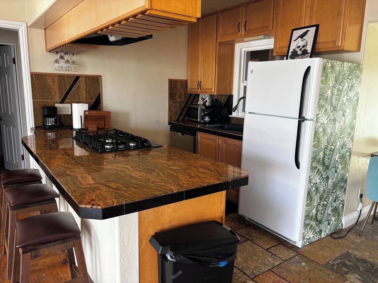 A kitchen with a central island, wooden cabinets, a white refrigerator, and a trash bin.