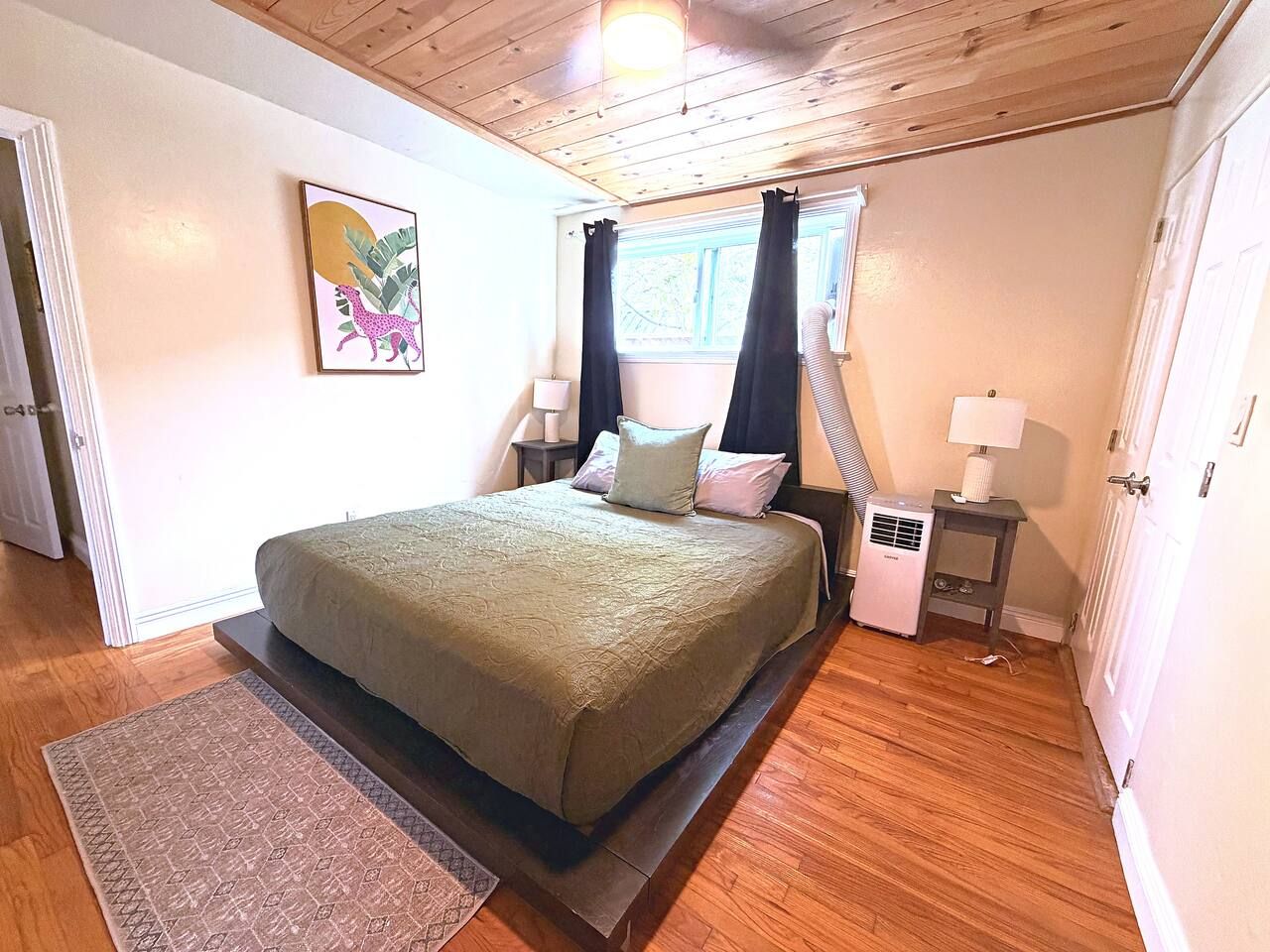 A bedroom with a bed, two bedside tables, a heater, and a window with curtains.
