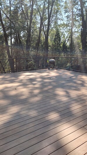 An outdoor deck with a barbecue grill, surrounded by trees.