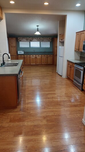 A kitchen with wooden cabinets, a stainless steel refrigerator, a built-in oven, and a wooden floor.