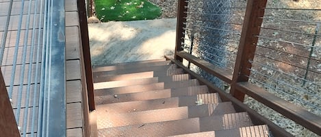 A wooden staircase with metal railings leading to a grassy area surrounded by trees.