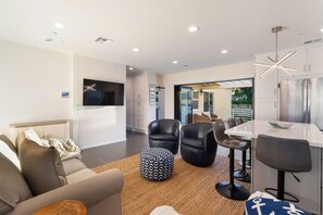 Una sala moderna con televisor de pantalla plana, sillas de cuero, una mesa de comedor y una cocina con refrigerador de acero inoxidable.