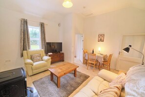 A living room with a sofa, a coffee table, a television, and a dining area with a table and chairs. - Cosy Irish Cottage in Navan with Fire & Large Garden (Navan)