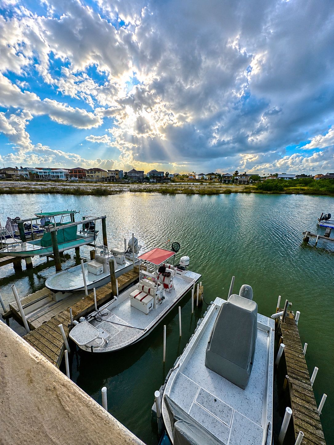 A marina with boats docked, a pier extending into calm water, and a distant shoreline with buildings.