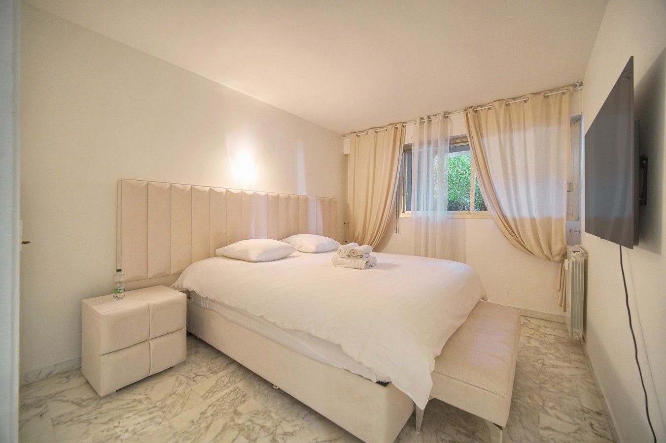 Ein Schlafzimmer mit einem Bett, Nachttischen, einem Fernseher und einem Fenster mit Vorhängen.