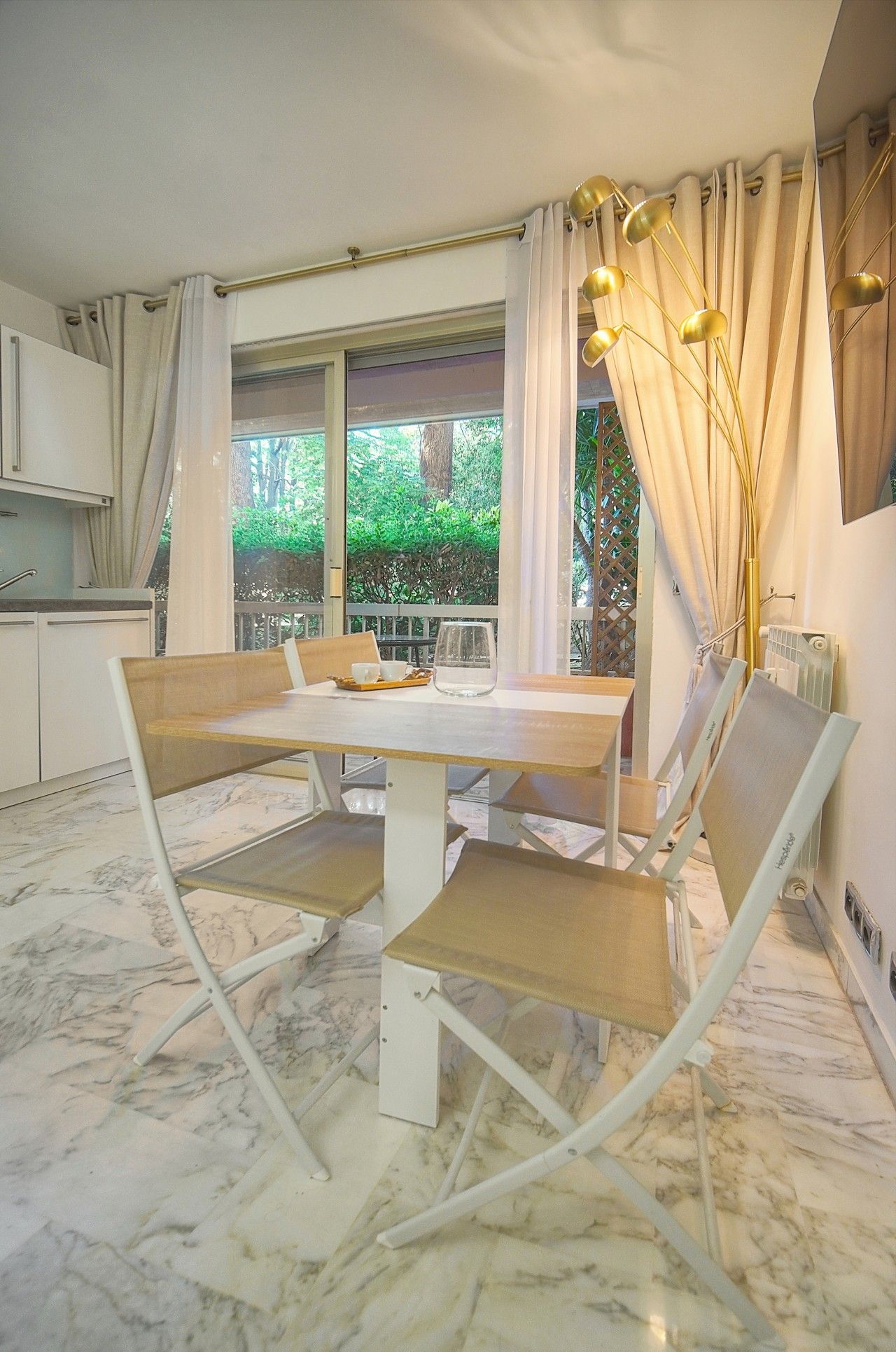 A dining area with a marble floor, a table with chairs, and a view of greenery outside.