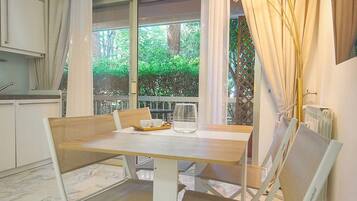 A dining area with a marble floor, a table with chairs, and a view of greenery outside.