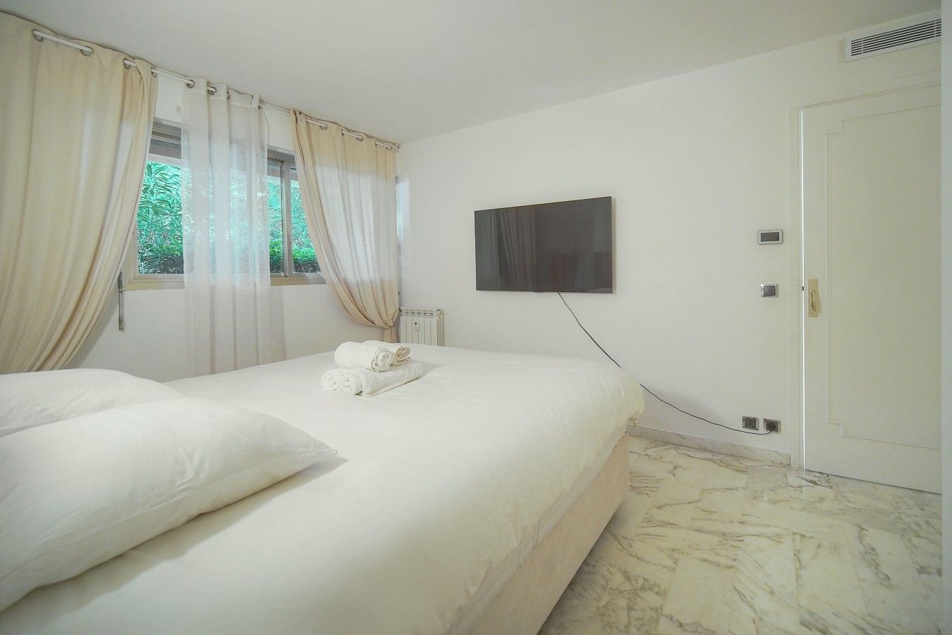 A hotel room with a bed, a flat-screen TV mounted on the wall, and a door.