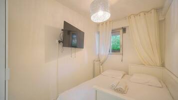 A bedroom with a bed, a TV mounted on the wall, a window with curtains, and a radiator.