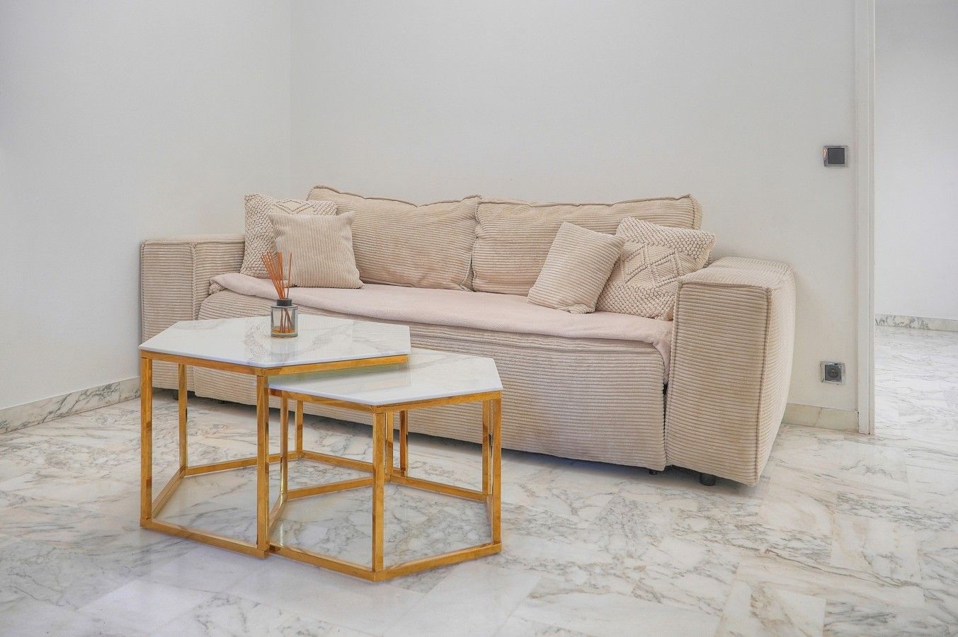 Ett minimalistiskt rum med en beige soffa, ett vitt marmorbord och ett marmorgolv.