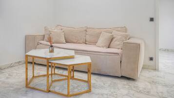 Ett minimalistiskt rum med en beige soffa, ett vitt marmorbord och ett marmorgolv.