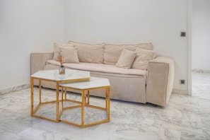 Ett minimalistiskt rum med en beige soffa, ett vitt marmorbord och ett marmorgolv.