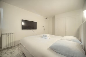 Ett hotellrum med en säng, en tv som är monterad på väggen, ett element och en dörr.