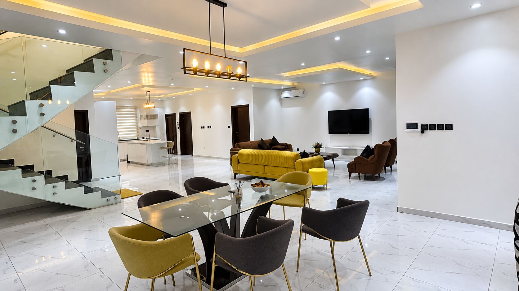 Un interior moderno con una mesa de comedor de vidrio, sillas, un sofá y una escalera.