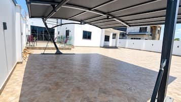Un patio couvert avec un sol carrelé, des sièges d’extérieur et une vue sur un bâtiment moderne.