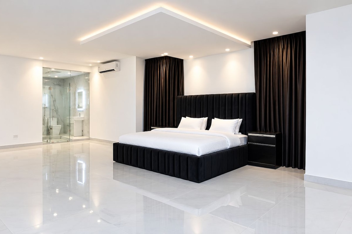 A modern bedroom with a large bed, a bedside table, and a glass shower area.
