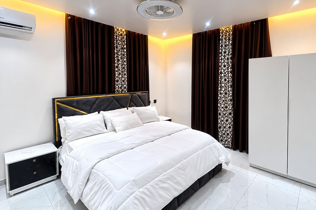 A modern bedroom with a bed, nightstands, a wardrobe, and an air conditioning unit.