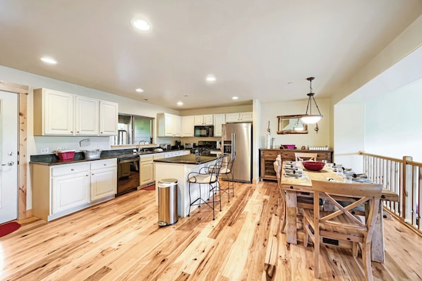 A modern kitchen with wooden flooring, white cabinetry, stainless steel appliances, and a dining area with a wooden table and chairs. - Bear Hollow Beauty. Hottub Walk to Free Bus 5435 (Park City)