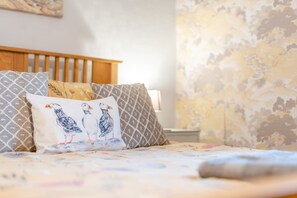 A bed with patterned pillows and a blanket, a wooden headboard, and a wall with a floral wallpaper. - Silverdale Cottage-Beach, Shop and Pub all nearby. Dog Friendly (Haverigg)