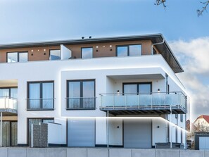 Ein modernes Mehrfamilienhaus mit Balkonen, großen Fenstern und einer Garage.