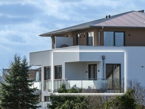 Un edificio residencial moderno de dos pisos con balcón, ventanas amplias y techo de metal.