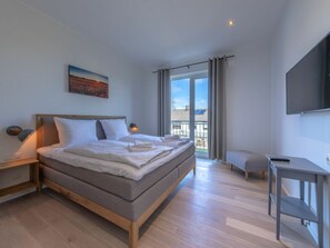 Ein modernes Schlafzimmer mit Bett, Nachttischen, einem Schreibtisch und einem Fernseher.
