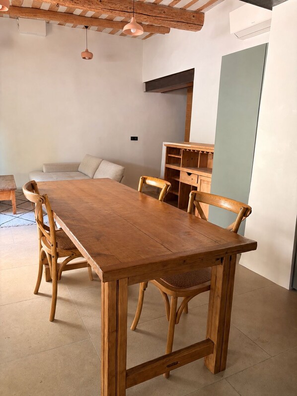 Ein Holztisch mit vier Stühlen, ein Holzschrank und eine hängende Pendelleuchte in einem Raum mit Fliesenboden und weißer Wand.