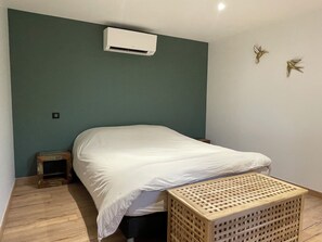 Ein Schlafzimmer mit einem Bett, einem kleinen Holzschemel, einer Holzkiste und einer Klimaanlage an der Wand.