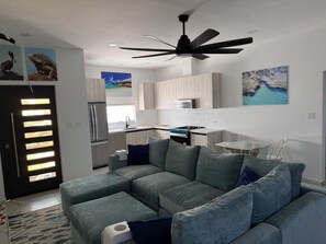 A modern living room with a sectional sofa, a ceiling fan, and artwork on the walls. - Aruban Charm | Private Pool | Seroe Janchi (Noord)
