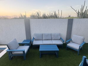 An outdoor seating area with a sofa and chairs, a small table, and a pool in the background. - Aruban Charm | Private Pool | Seroe Janchi (Noord)
