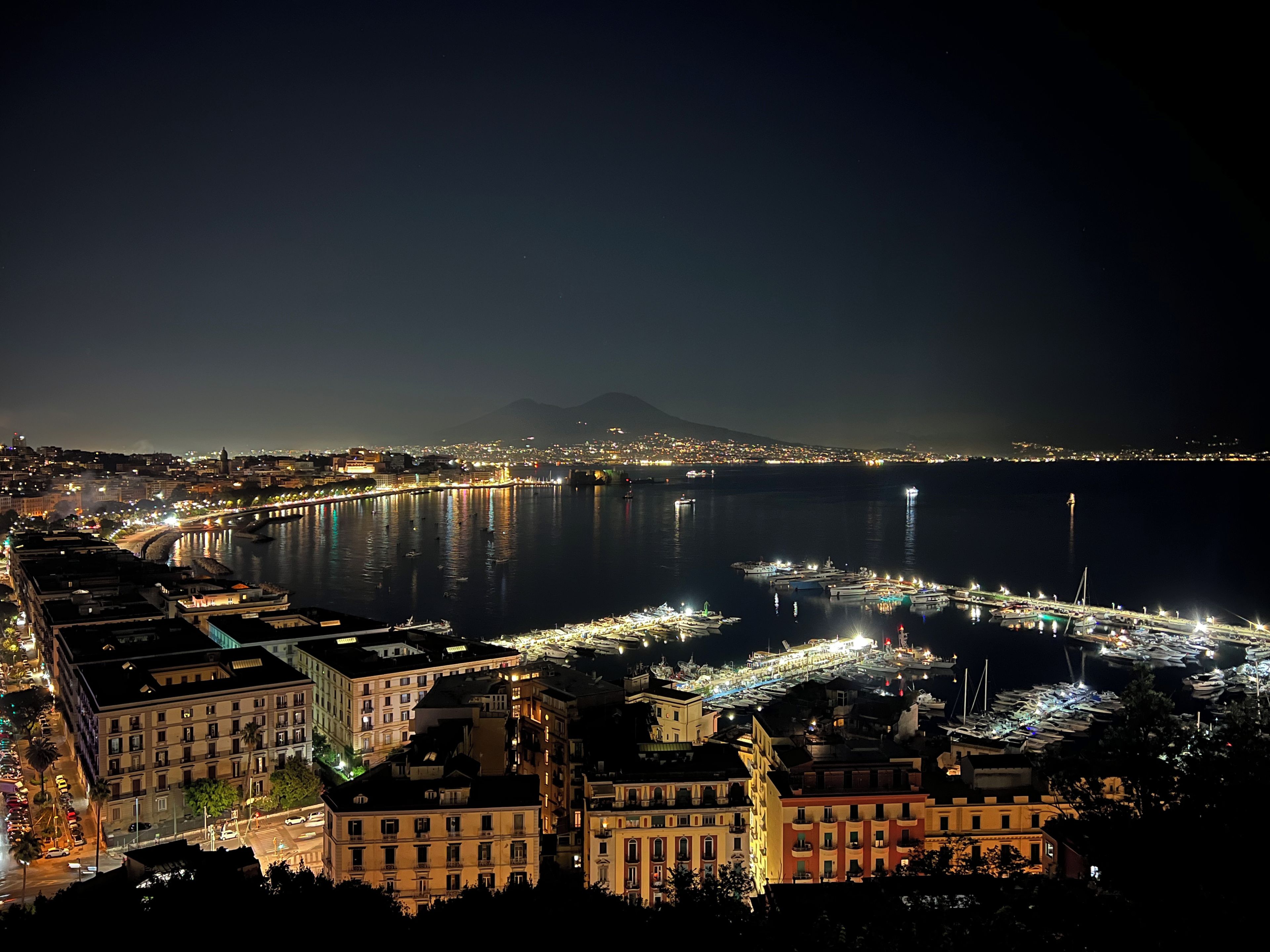 A nighttime cityscape with a river, buildings, and a distant mountain.