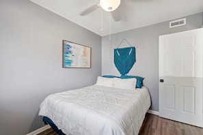 A bedroom with a bed, a wall-mounted artwork, a macrame wall hanging, and a white door. - 108 Latitude Adjustment (Murrells Inlet)