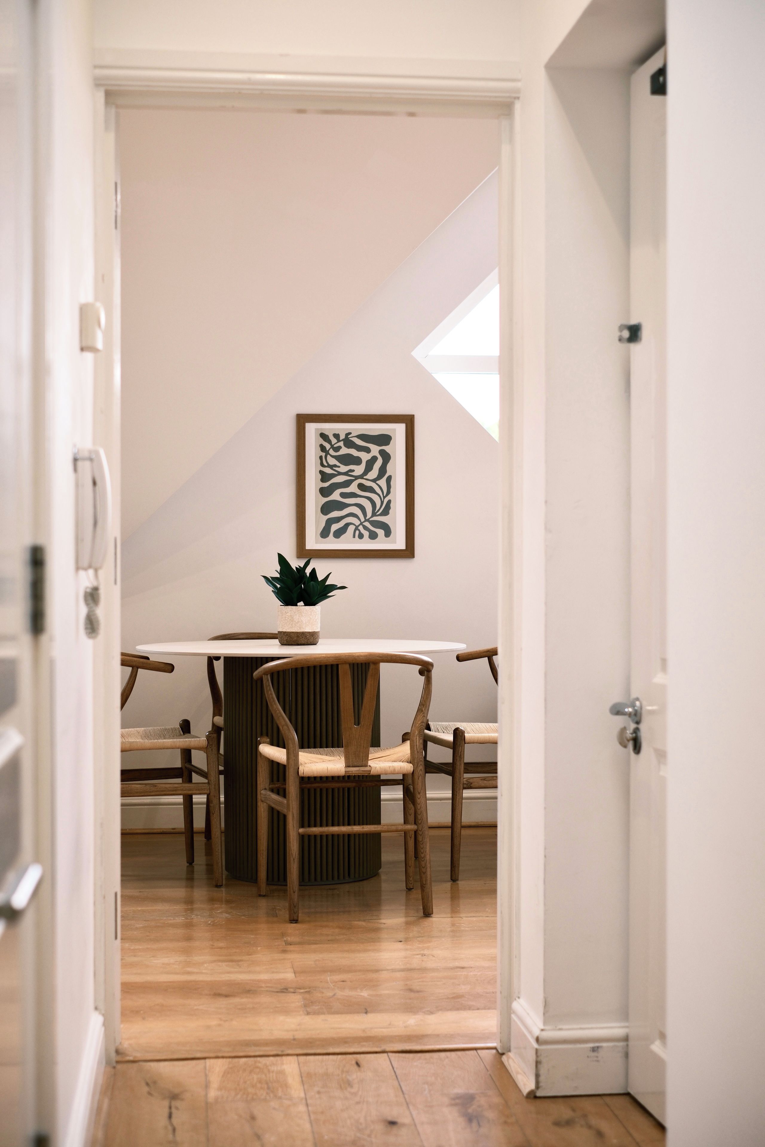 Una habitació amb taula de dinar, cadires, una planta en test i una obra d'art emmarcada a la paret.