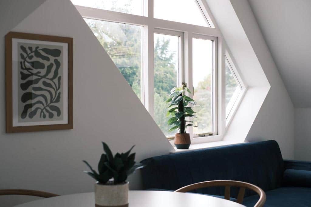 Een kamer met een eettafel, stoelen, een blauwe bank, een potplant en een ingelijste afbeelding aan de muur.