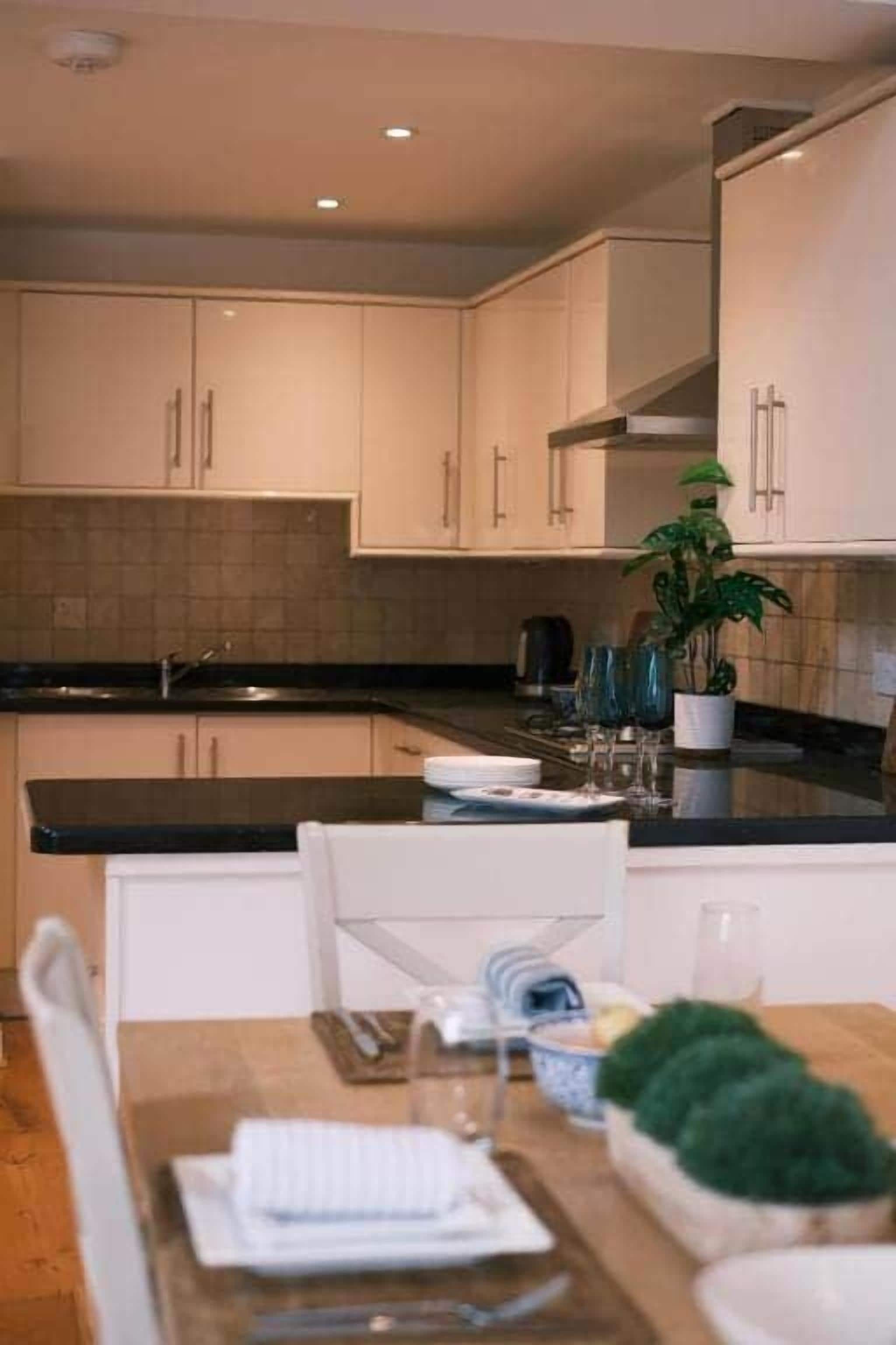A modern kitchen with white cabinets, a black countertop, and a dining area with a table set for two.